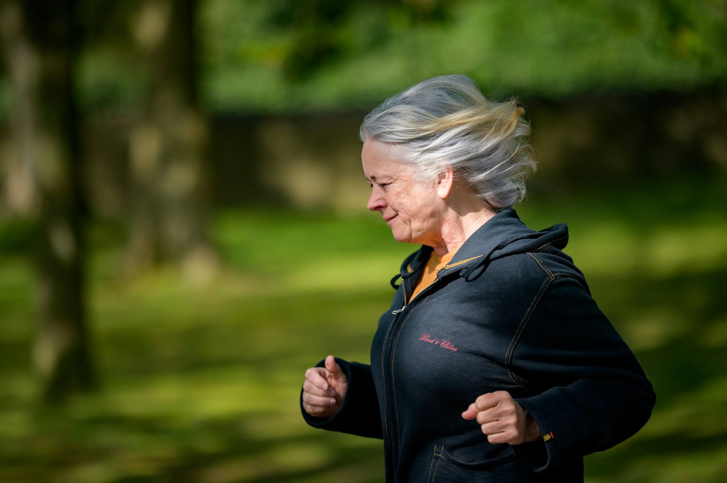 A gray-haired woman jogging through a green park